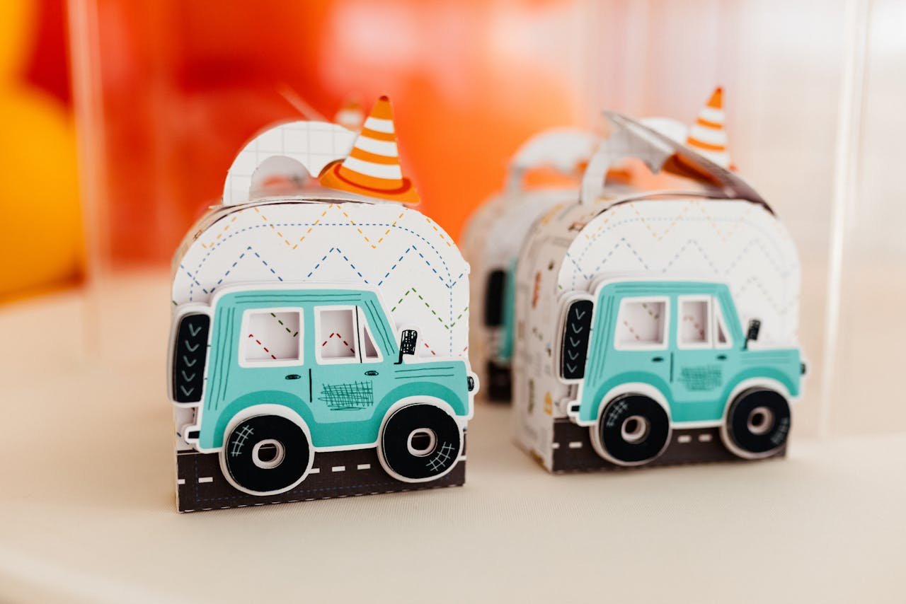 hero-img-01 Colorful toy car-themed gift boxes with party hats, ideal for kids' birthday parties or festive events.
